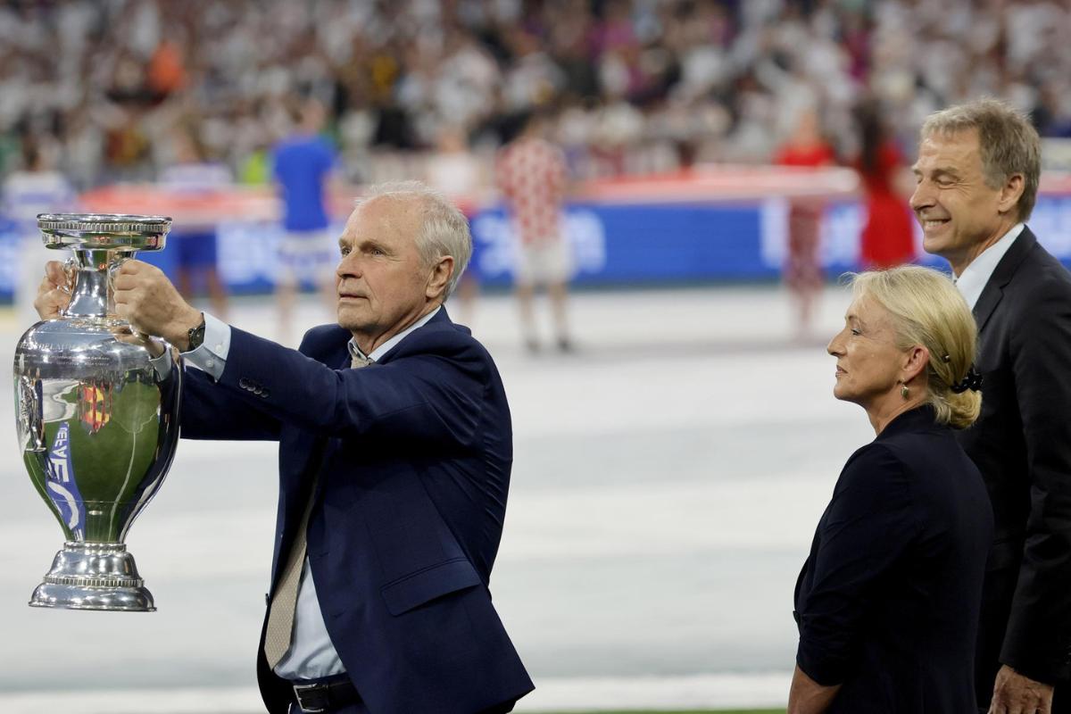 Bernard Dietz (izq.), Juergen Klinsmann (der.) y Heidi Beckenbauer, viuda del fallecido Franz Beckenbauer, traen al terreno de juego la Copa Henri Delaunay antes del partido Alemania y Escocia en Múnich, en la Eurocopa 2024.