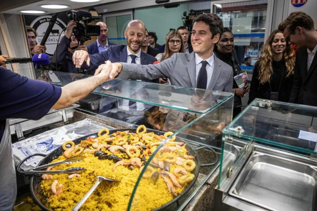 El primer Ministro francés Gabriel Attal (C) visita un mercado de alimentos con el candidato del partido mayoritario presidencial.